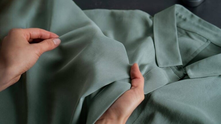 Χέρια που κρατούν ένα πράσινο πουκάμισο για έλεγχο μετά το πλύσιμο