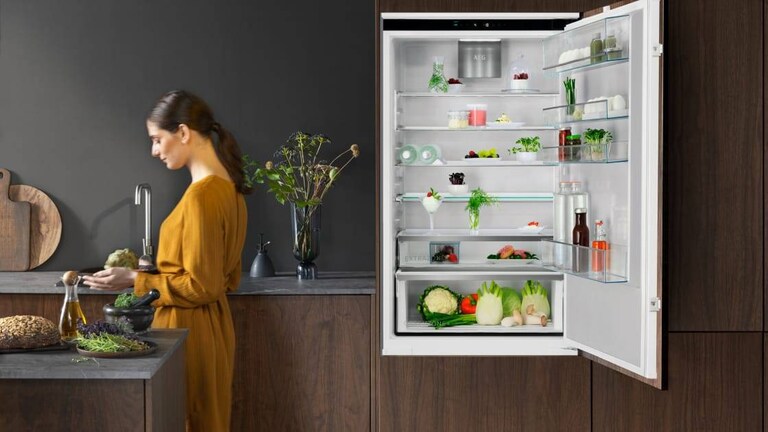 Γυναίκα στέκεται σε μια κουζίνα AEG με την πόρτα του ψυγείου ανοιχτή